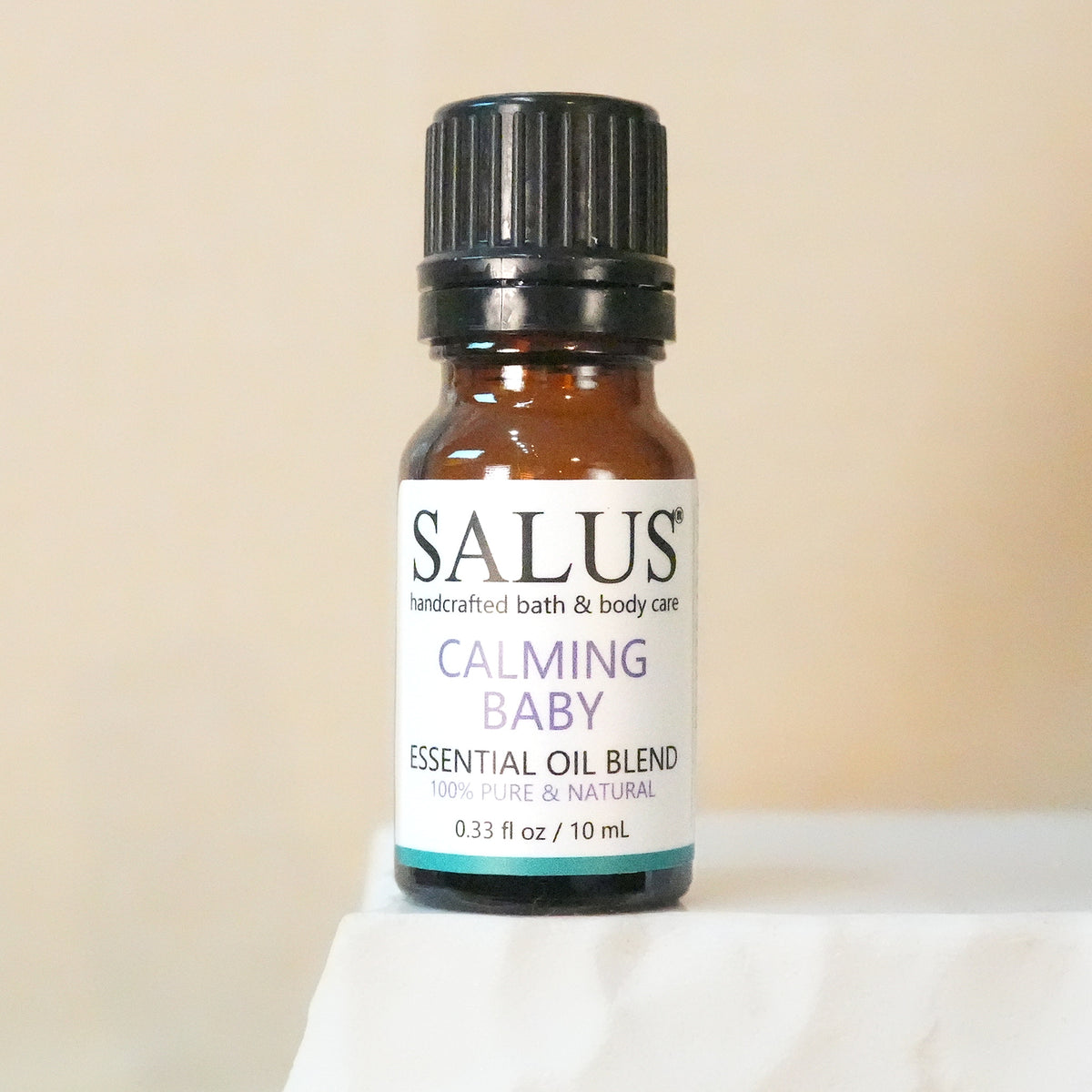 SALUS Calming Baby essential oil blend, 10 mL amber bottle on a white stone pedestal.