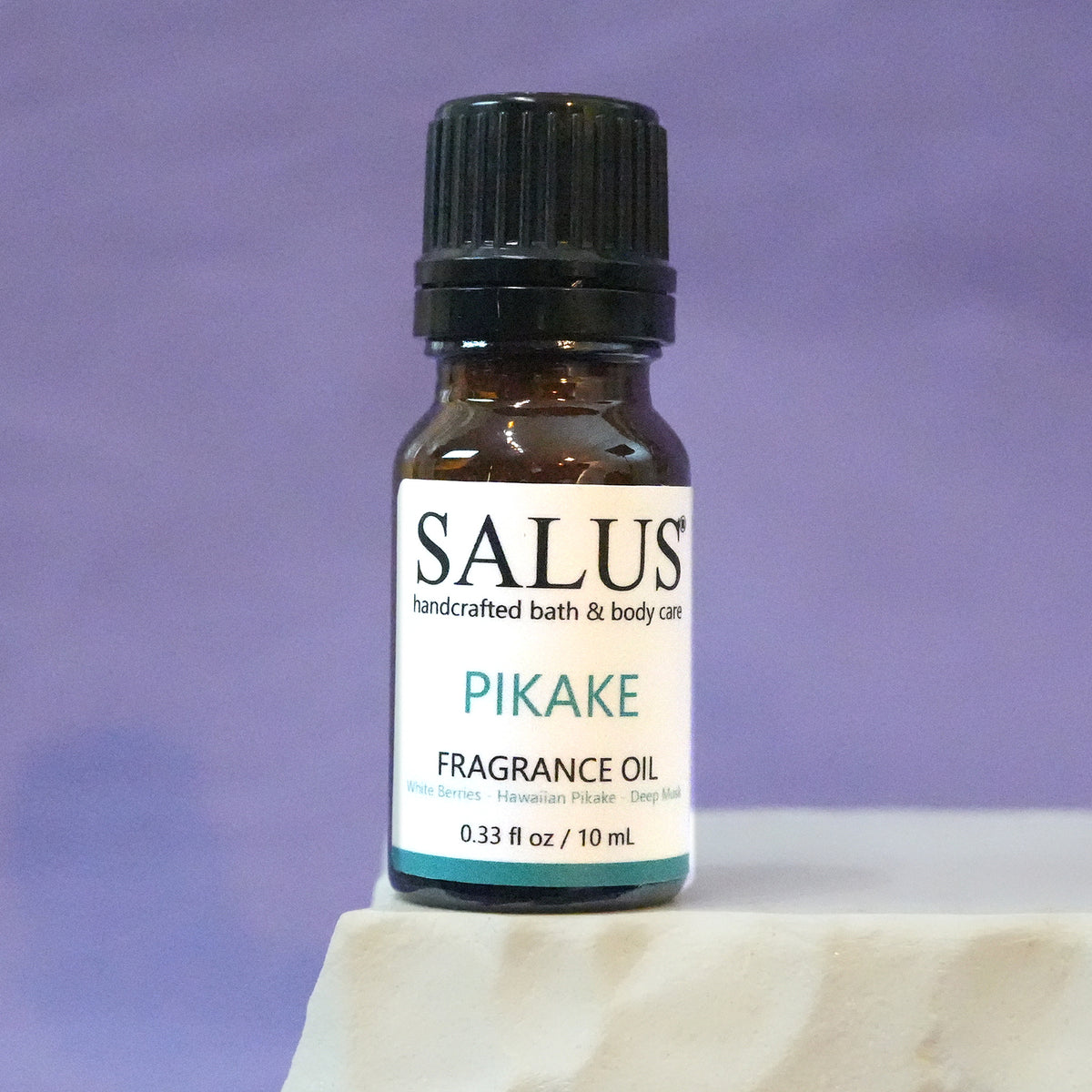 SALUS Pikake fragrance oil, 10 mL amber bottle on a white stone pedestal.