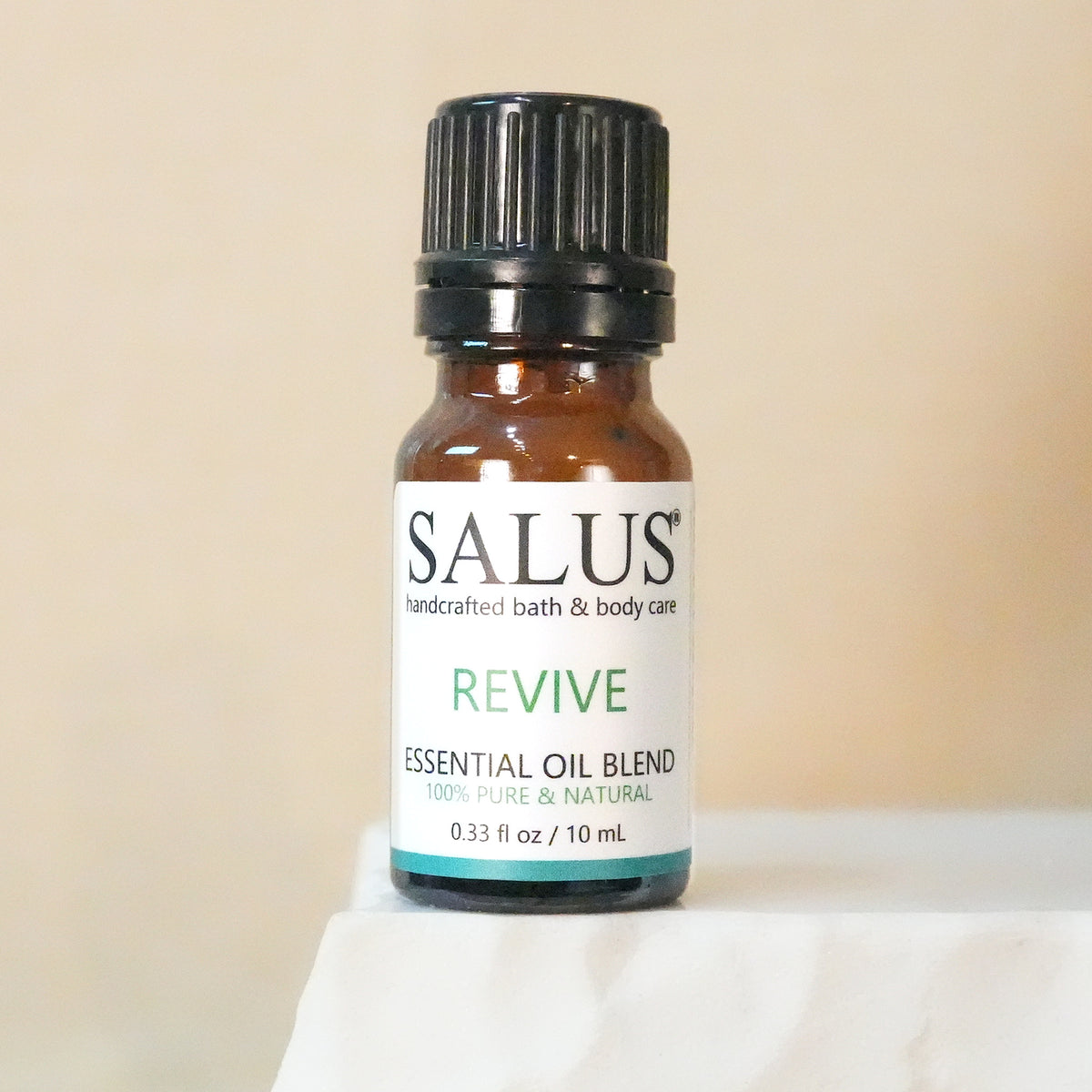 SALUS Revive essential oil blend, 10 mL amber bottle on a white stone pedestal.