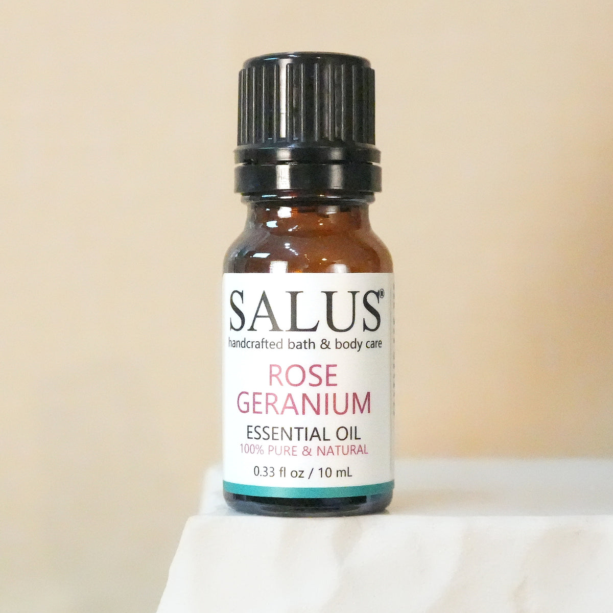 SALUS Rose Geranium essential oil, 10 mL amber bottle on a white stone pedestal.