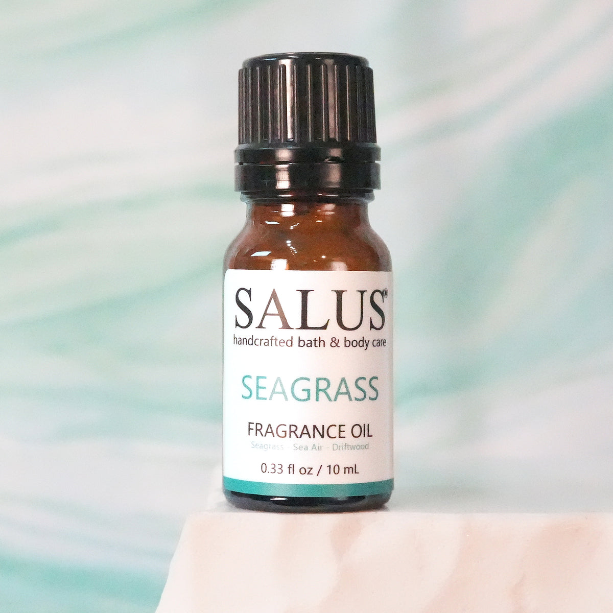 SALUS Seagrass fragrance oil, 10 mL amber bottle on a white stone pedestal.