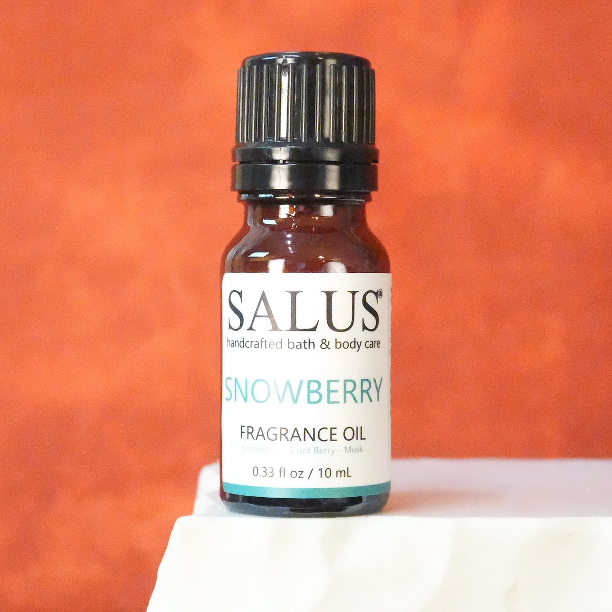 SALUS Snowberry fragrance oil, 10 mL amber bottle on a white stone pedestal.
