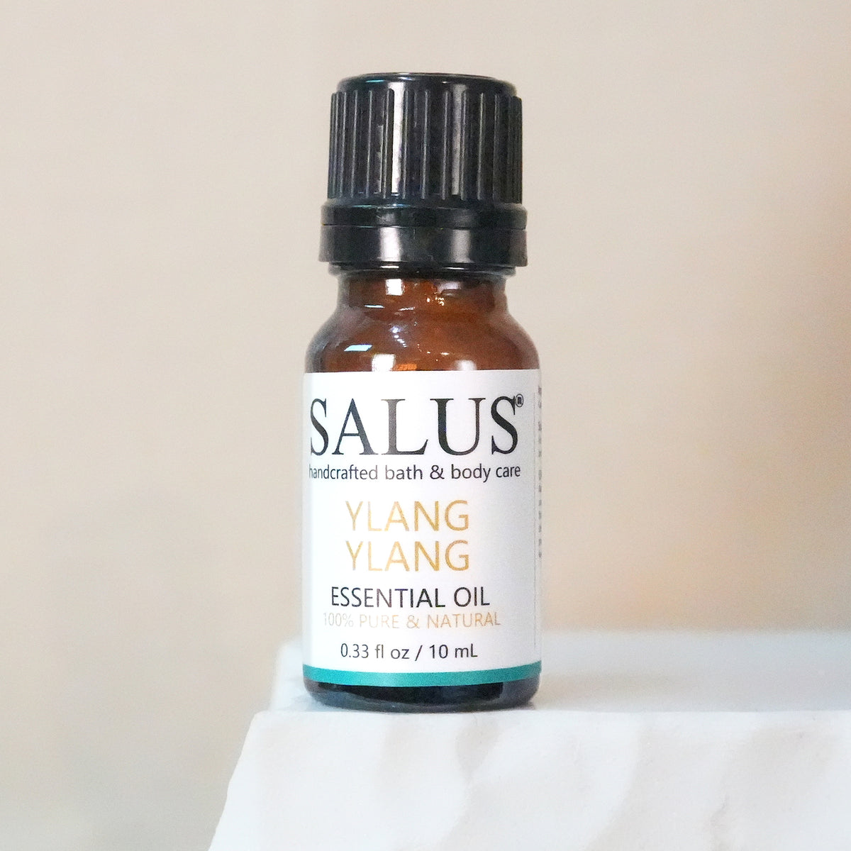 SALUS Ylang Ylang essential oil, 10 mL amber bottle on a white stone pedestal.