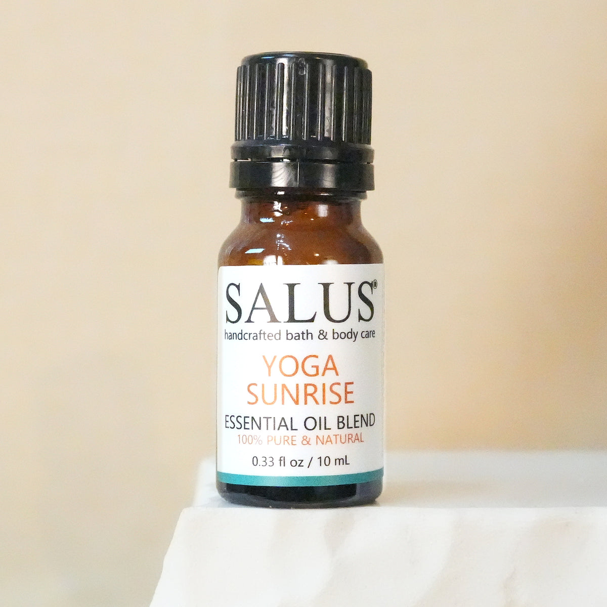 SALUS Yoga Sunrise essential oil blend, 10 mL amber bottle on a white stone pedestal.
