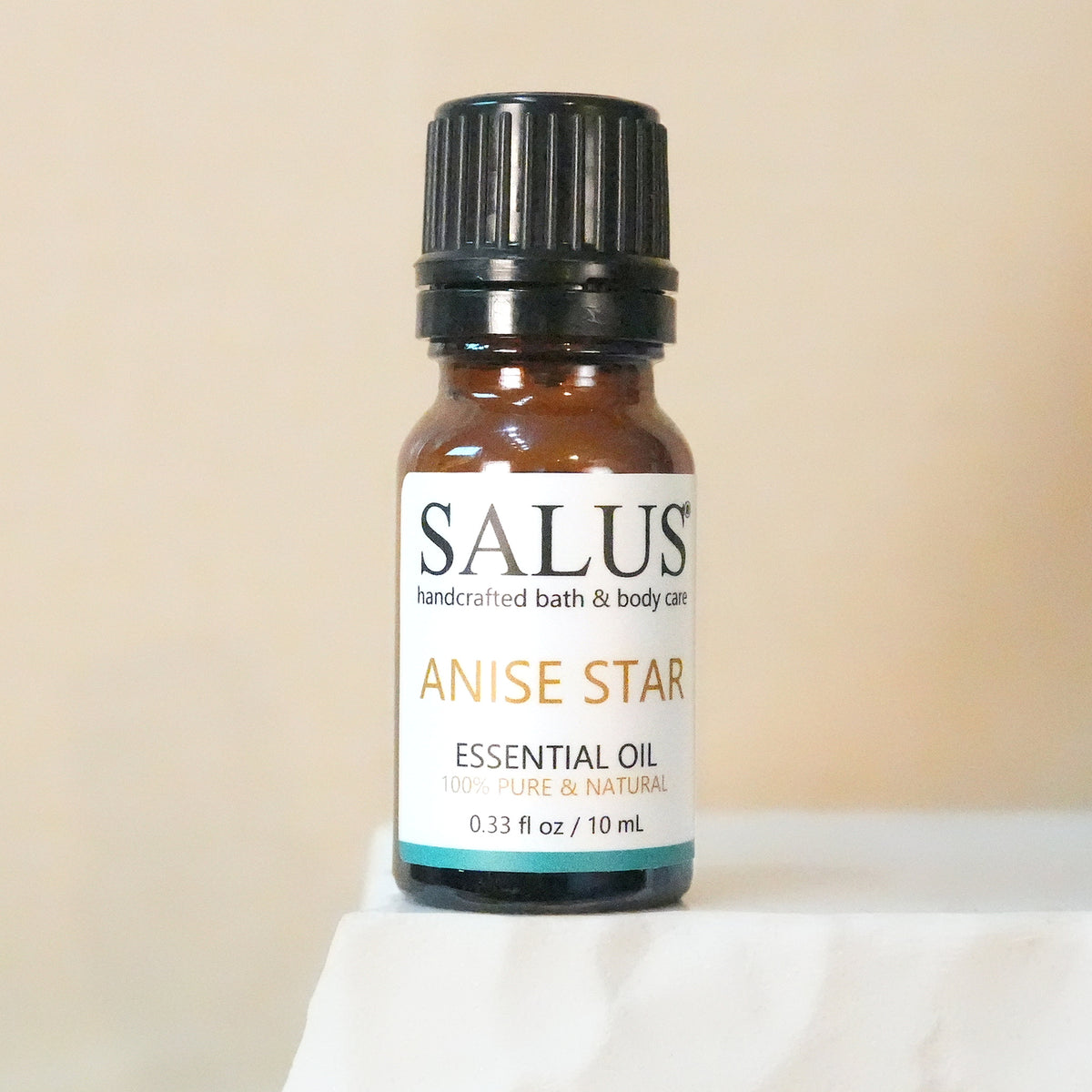 SALUS Anise Star essential oil, 10 mL amber bottle on a white stone pedestal.