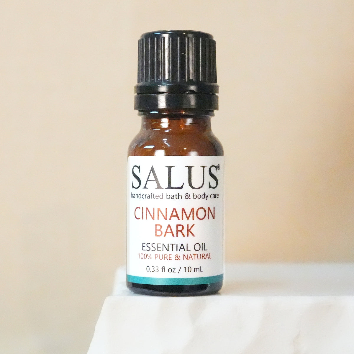 SALUS Cinnamon Bark essential oil, 10 mL amber bottle on a white stone pedestal.