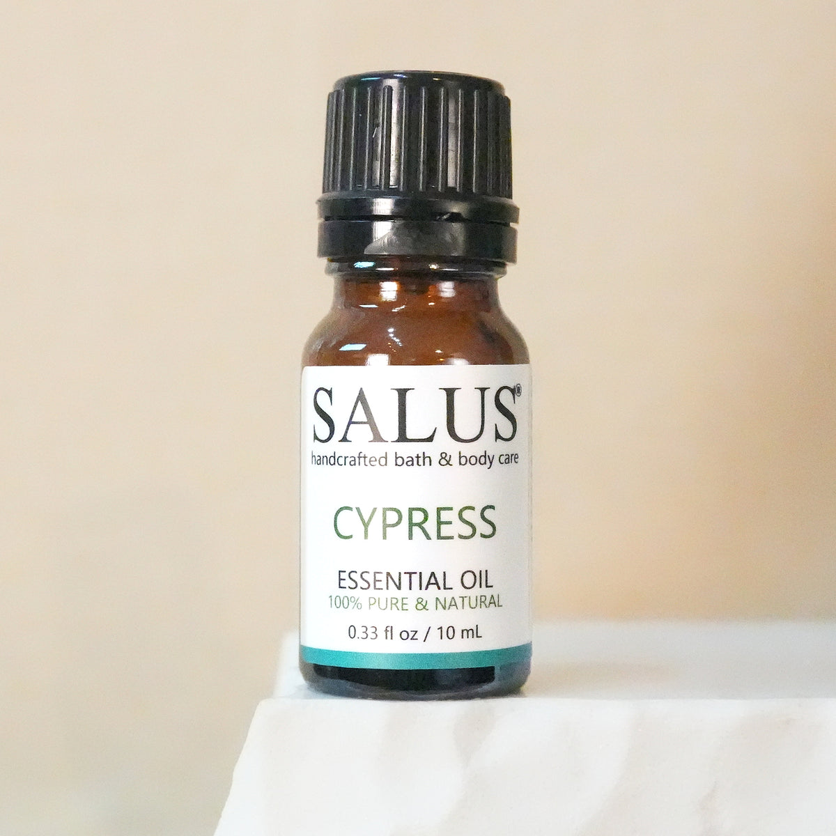 SALUS Cypress essential oil, 10 mL amber bottle on a white stone pedestal.