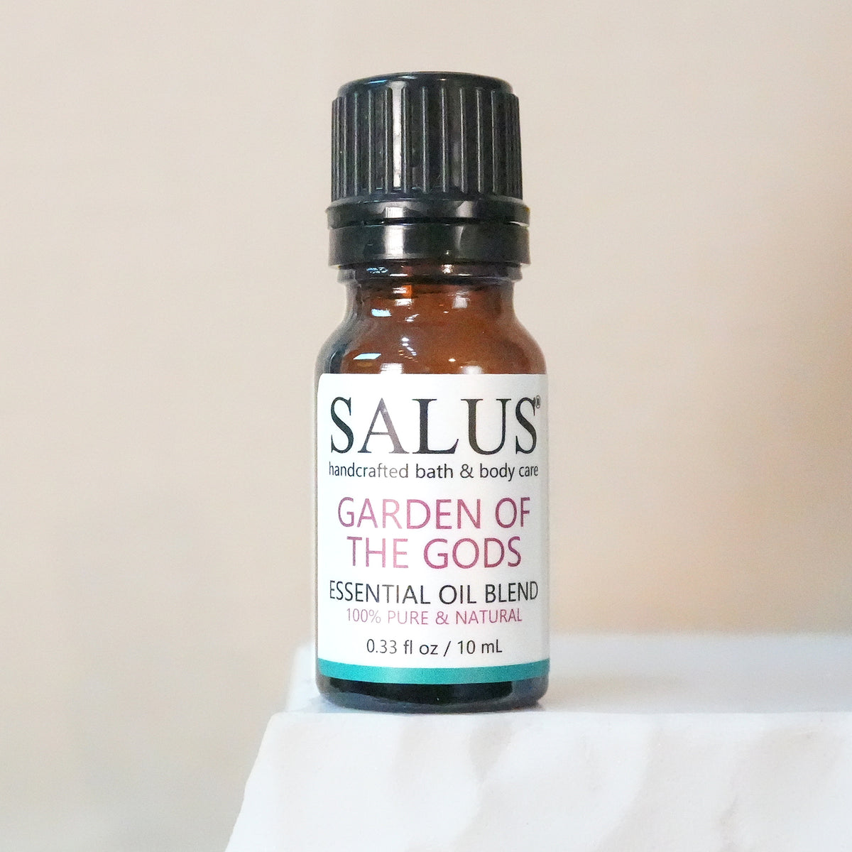 SALUS Garden of the Gods essential oil blend, 10 mL amber bottle on a white stone pedestal.
