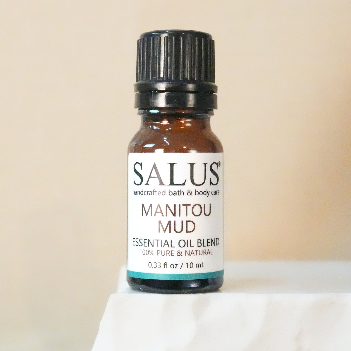 SALUS Manitou Mud essential oil blend, 10 mL amber bottle on a white stone pedestal.