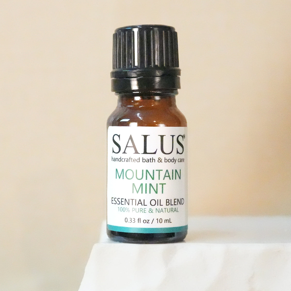 SALUS Mountain Mint essential oil blend, 10 mL amber bottle on a white stone pedestal.