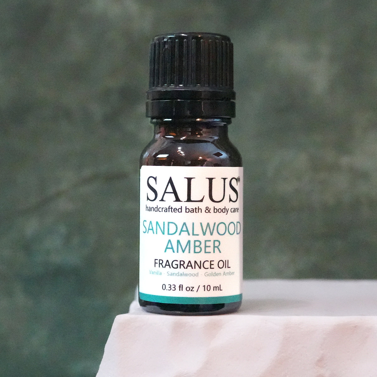 SALUS Sandalwood Amber fragrance oil, 10 mL amber bottle on a white stone pedestal.
