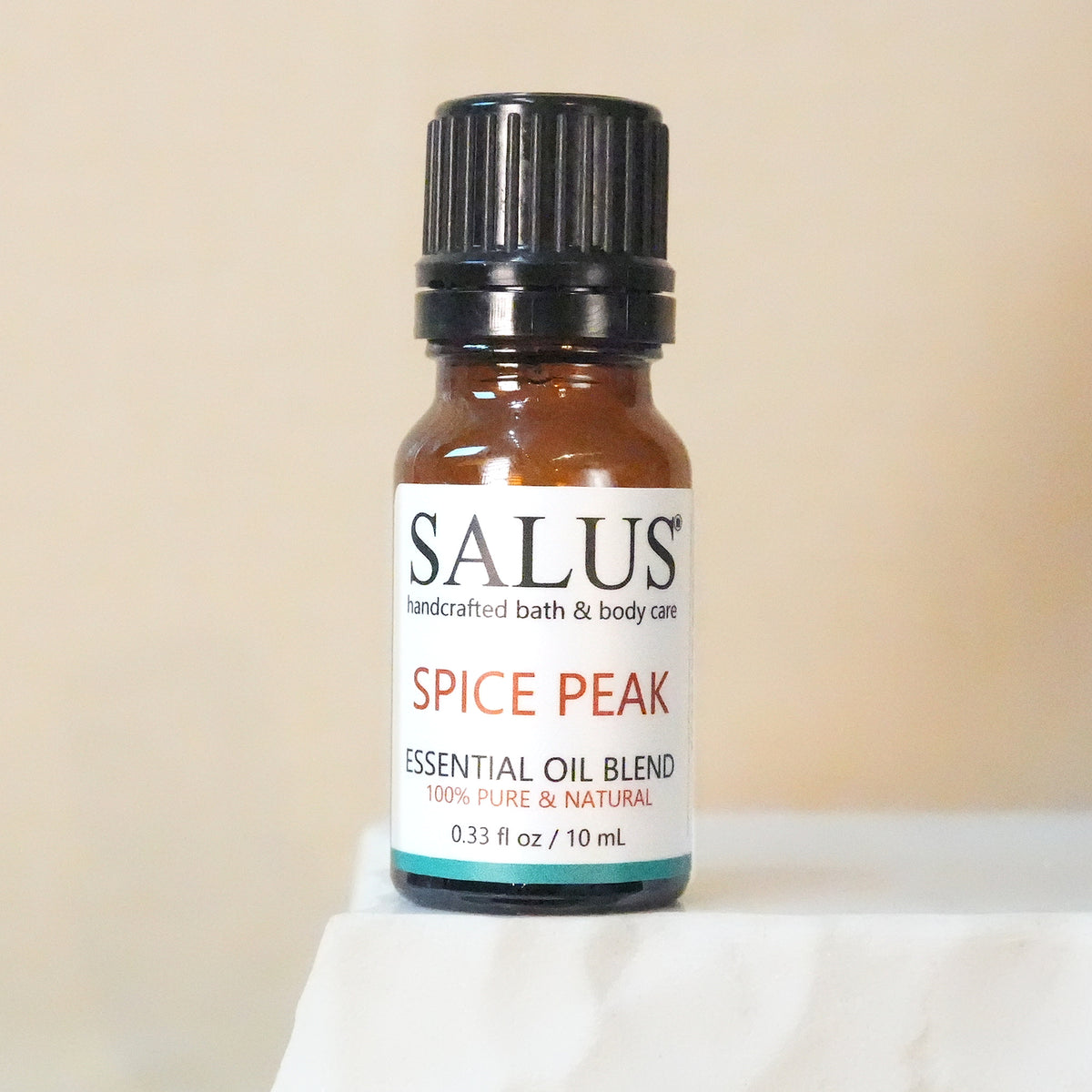 SALUS Spice Peak essential oil blend, 10 mL amber bottle on a white stone pedestal.