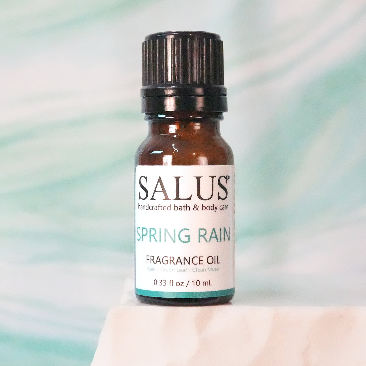 SALUS Spring Rain fragrance oil, 10 mL amber bottle on a white stone pedestal.