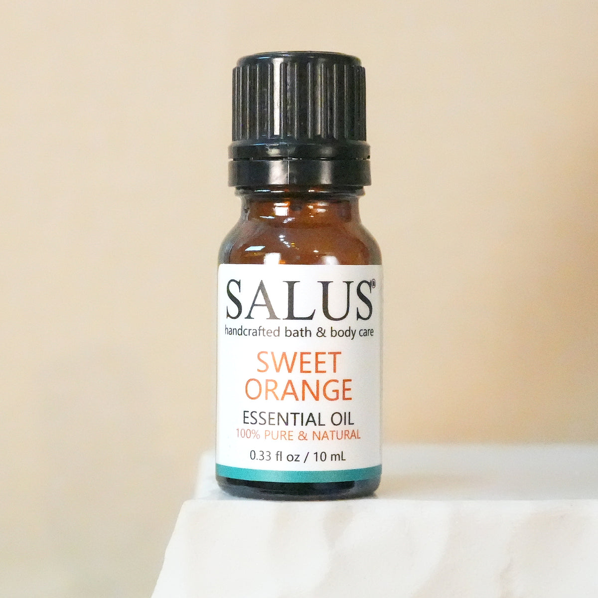 SALUS Sweet Orange essential oil, 10 mL amber bottle on a white stone pedestal.