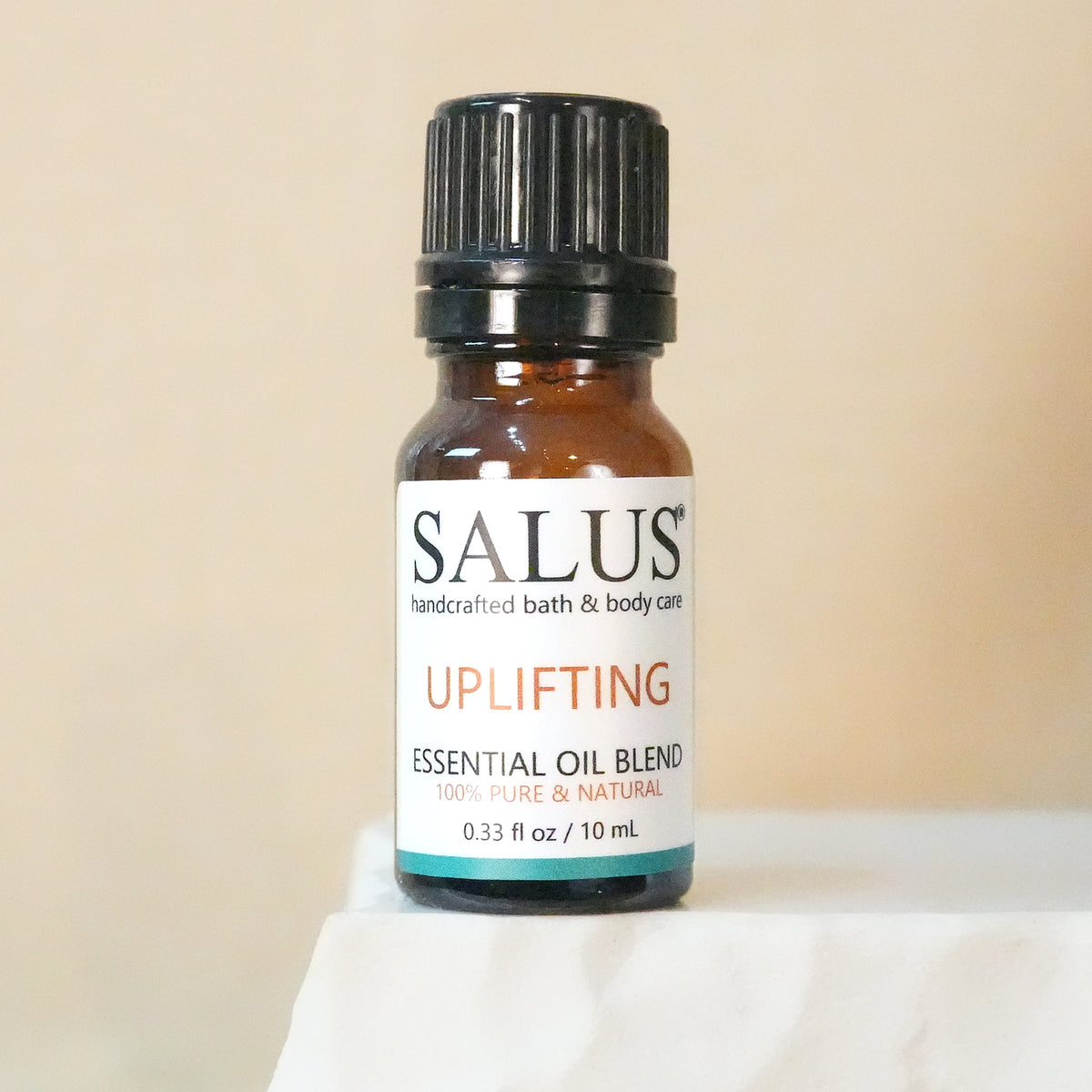 SALUS Uplifting essential oil blend, 10 mL amber bottle on a white stone pedestal.